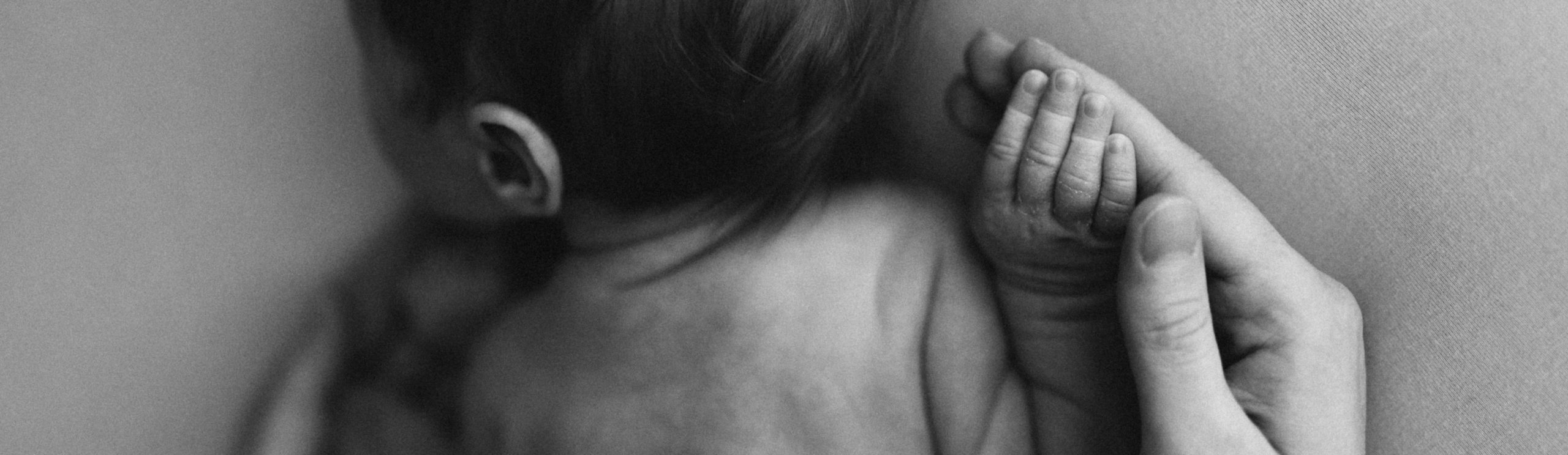 Новорожденный малыш держит руку родителя в черно-белом фото.